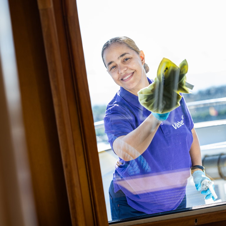 Weibliche Reinigungskraft putzt Fenster und lächelt in die Kamera