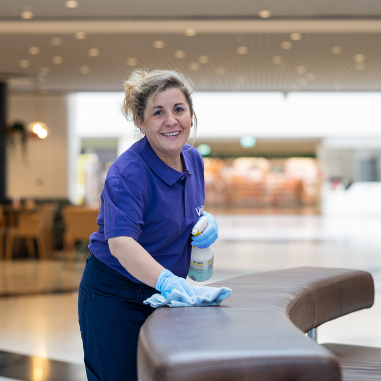 Weibliche Reinigungskraft reinigt Sitz und lächelt in die Kamera im Einkaufszentrum 