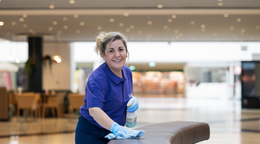 Weibliche Reinigungskraft reinigt Sitz und lächelt in die Kamera im Einkaufszentrum 