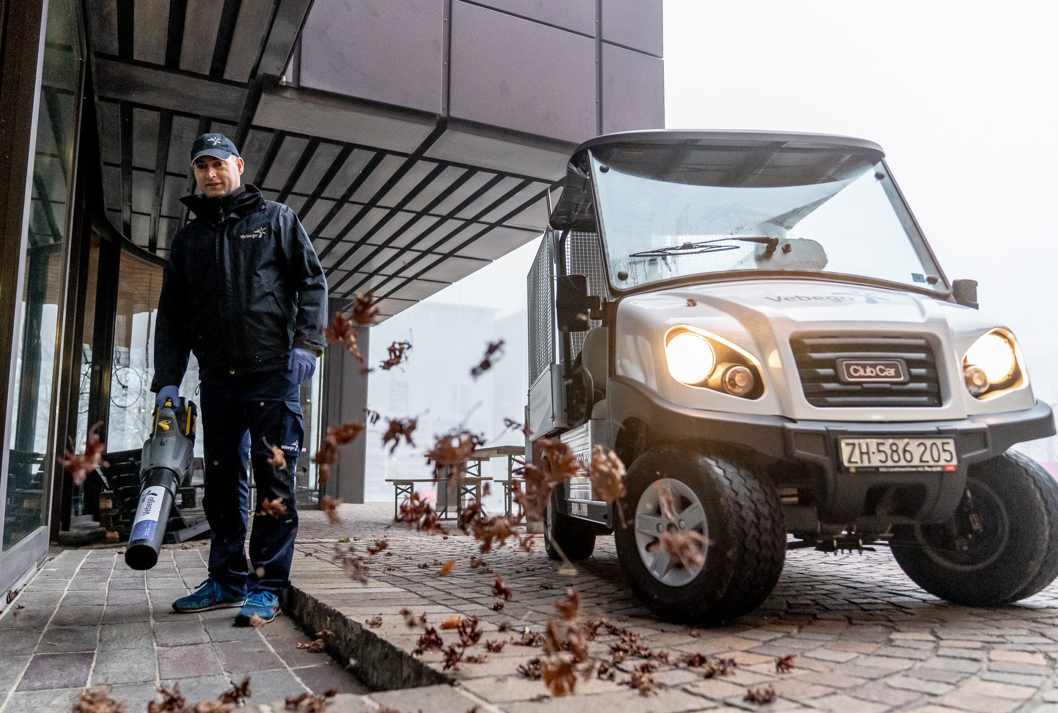 Hausmeister bläst Laub neben einem Golfcart